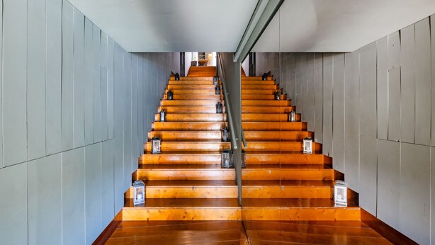 A wooden staircase with a metal handrail and lantern-style lights on each step.