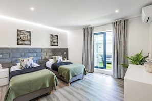 Quarto de hotel moderno com duas camas, uma janela grande com cortinas, uma planta e arte na parede.