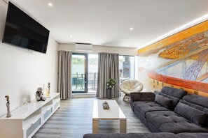 Uma sala de estar moderna com televisão de tela plana, um sofá, uma mesa de centro e um quadro grande.