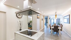 A modern kitchen with a built-in stove, a dining area with a wooden table and chairs, and a large window with curtains.