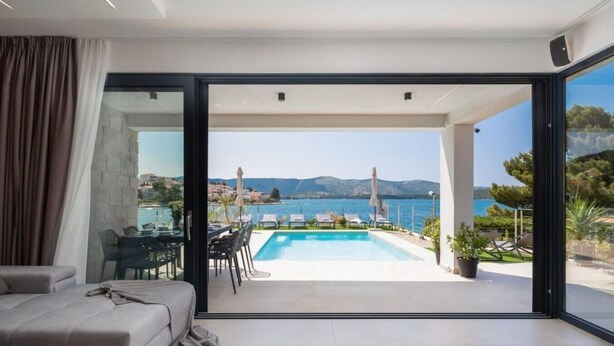 A modern living room with a large sliding glass door leading to an outdoor pool area with a scenic view of the sea and mountains. - Villa Dragica - Private villa with pool, Sibenik (Zaboric)
