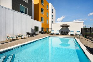 Piscina com espreguiçadeiras e mesas, cercada por um edifício com fachada branca e laranja.