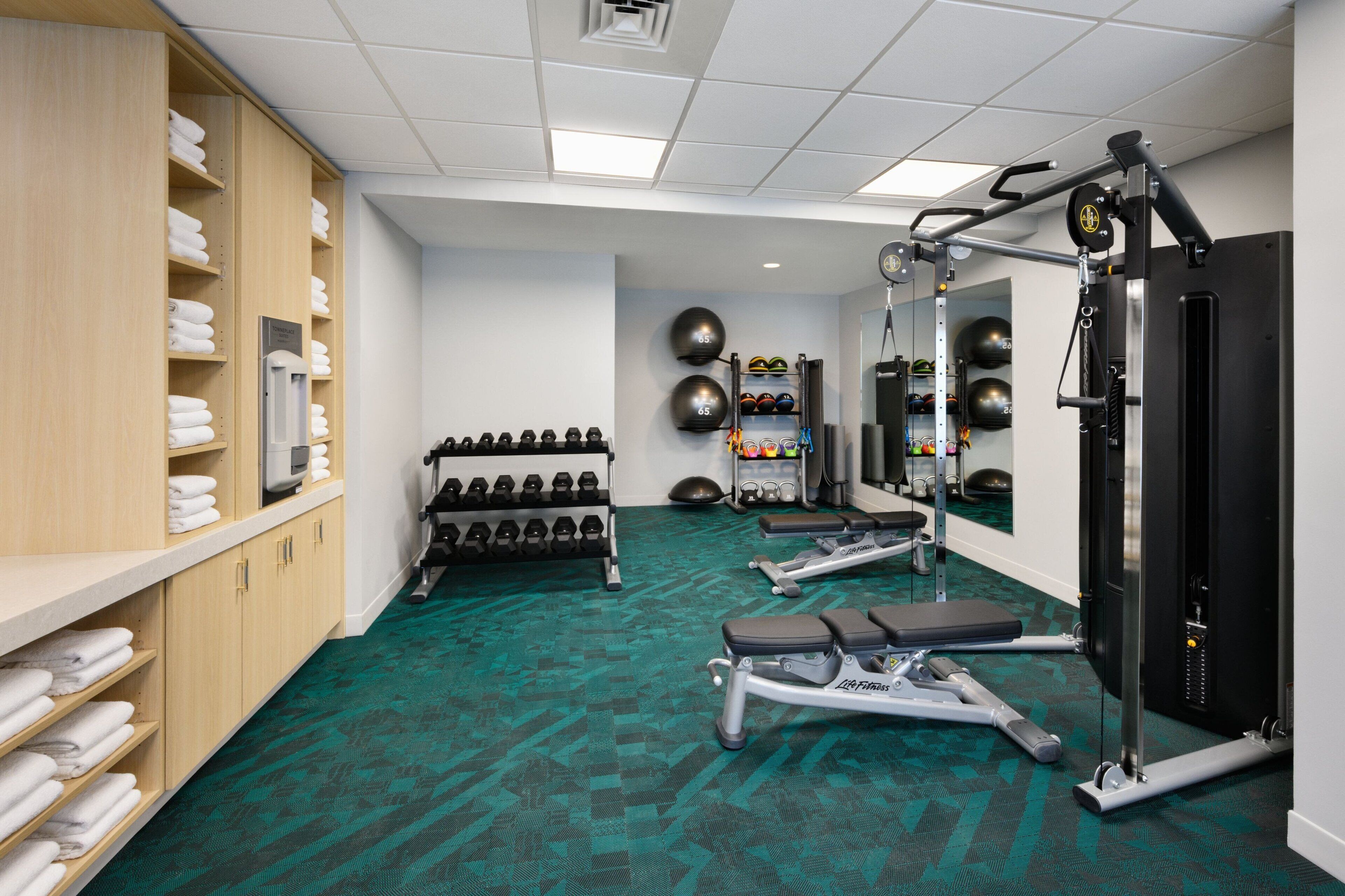 A gym with exercise equipment, a rack of dumbbells, and a wall-mounted medicine ball rack.