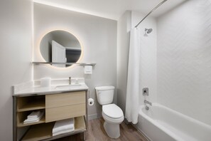 Uma casa de banho moderna com sanita, lavatório, espelho e banheira.