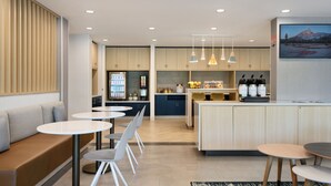 A modern kitchen with a central island, a seating area with round tables, and a refrigerator.