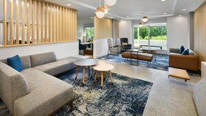 A modern hotel lobby with a sofa, chairs, a coffee table, and a patterned rug.