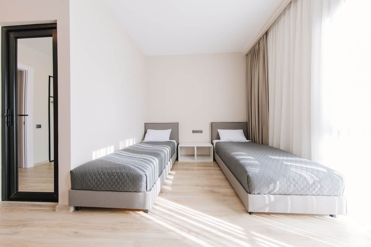 A modern bedroom with two single beds, a wooden floor, and a large mirror.