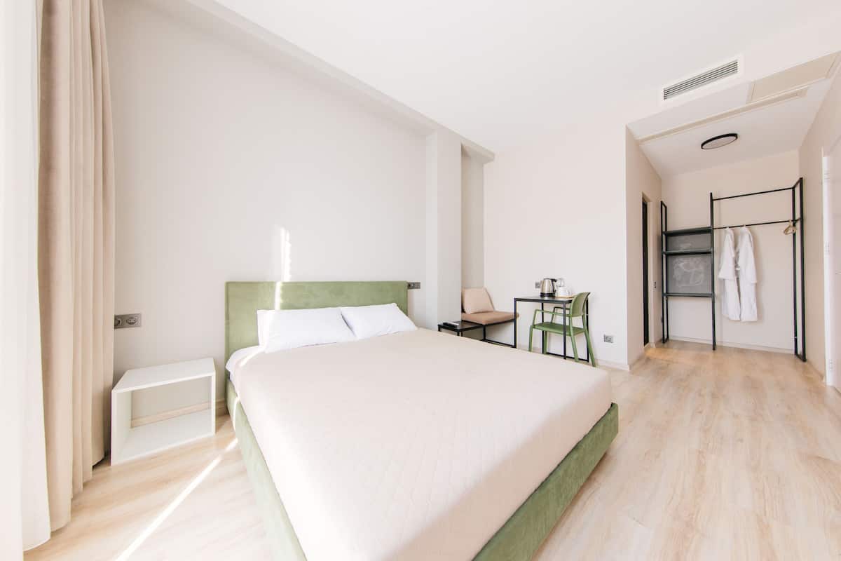 A modern hotel room with a large bed, a small desk, and a walk-in closet.