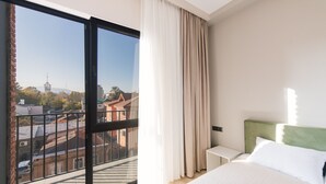 A hotel room with a large window, a bed with white bedding, a green headboard, and a small bedside table. - Doors Hotel (Tbilisi)