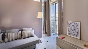 A modern hotel room with a sofa, a lamp, a framed artwork, and a view of the city through large windows. - City and the Sea in Genova (Genoa)