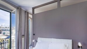 A hotel room with a large window, a bed with white linens, a nightstand with a lamp, and a view of buildings outside. - City and the Sea in Genova (Genoa)