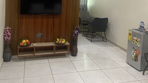 A living room with a wooden entertainment unit, a flat-screen TV, a dining area with a table and chairs, and a refrigerator with magnets. - ULTIMATE HOTEL (Mile 11)