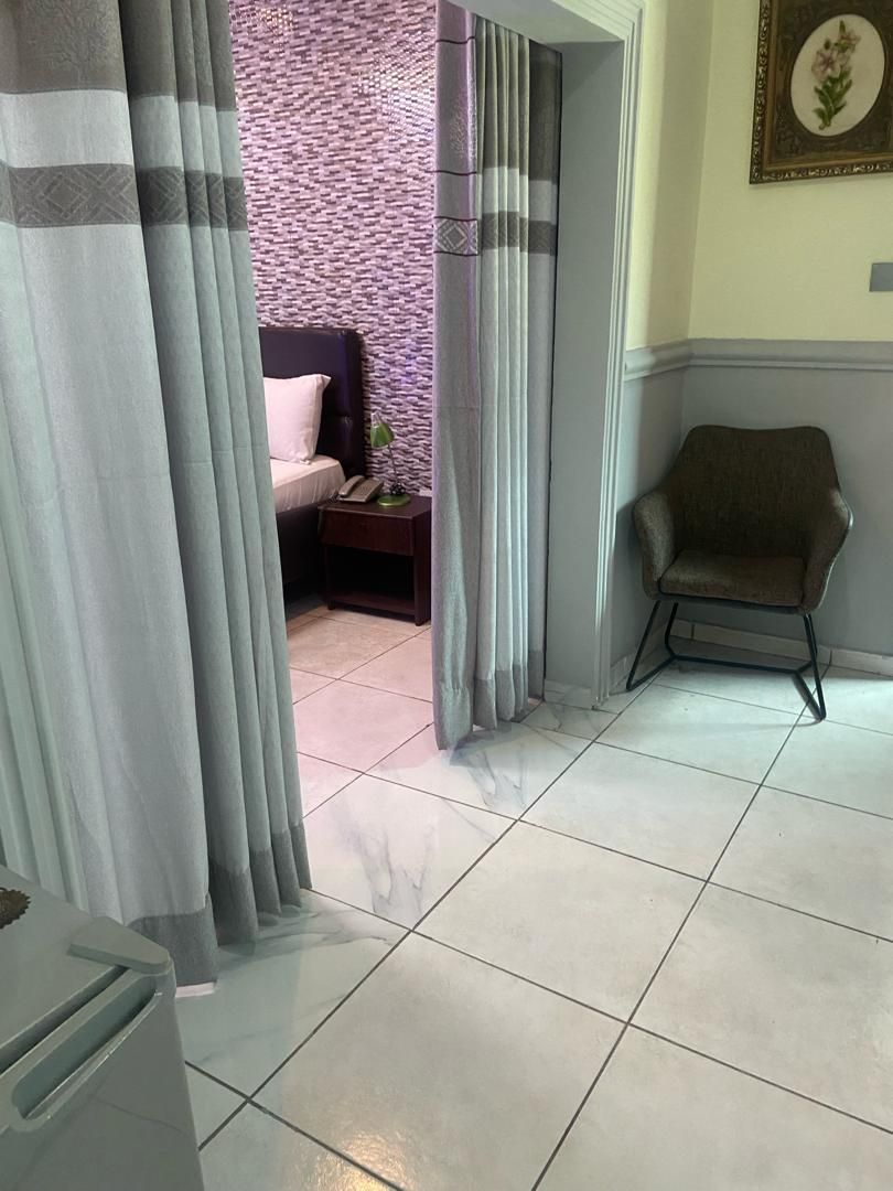 Una habitación con cama, mesita de noche, silla y cortina.