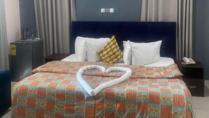 A hotel room with a bed, curtains, an air conditioning unit, a bedside table, and a telephone. - ULTIMATE HOTEL (Mile 11)