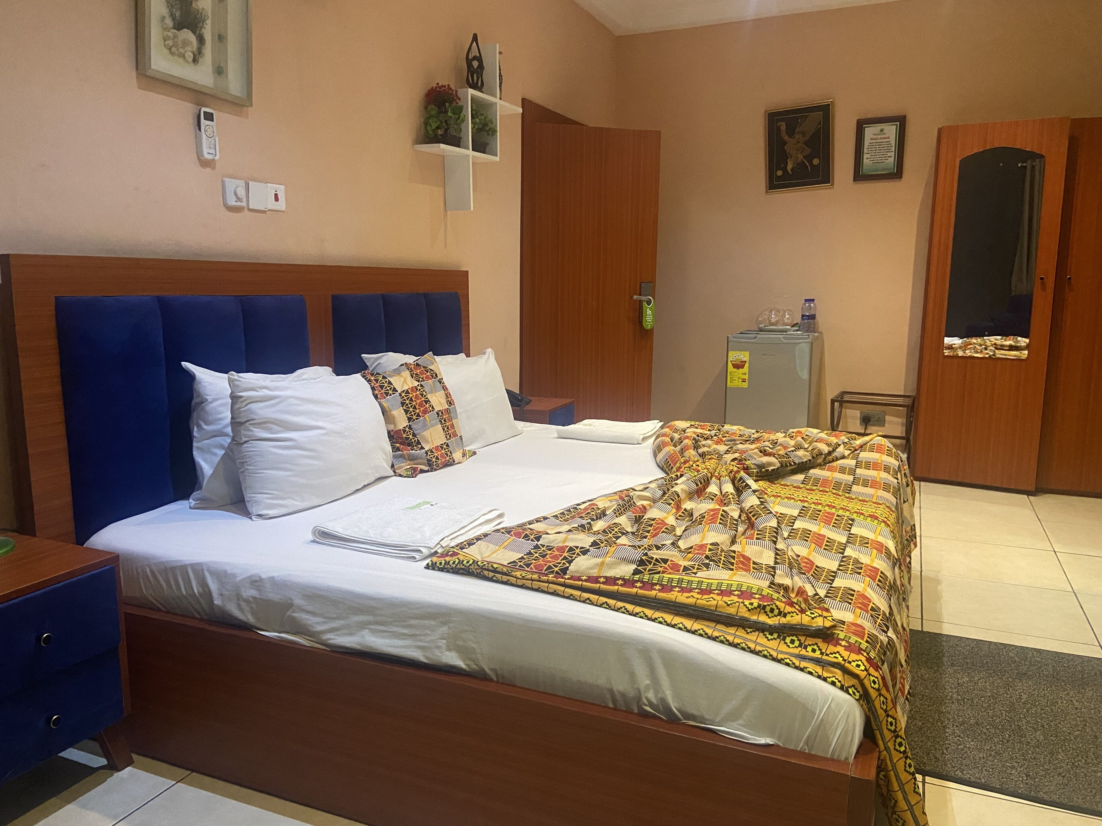 Ein Hotelzimmer mit einem großen Bett, einem Holz-Kopfteil, einem kleinen Schreibtisch, einem Kleiderschrank und einem Kühlschrank.