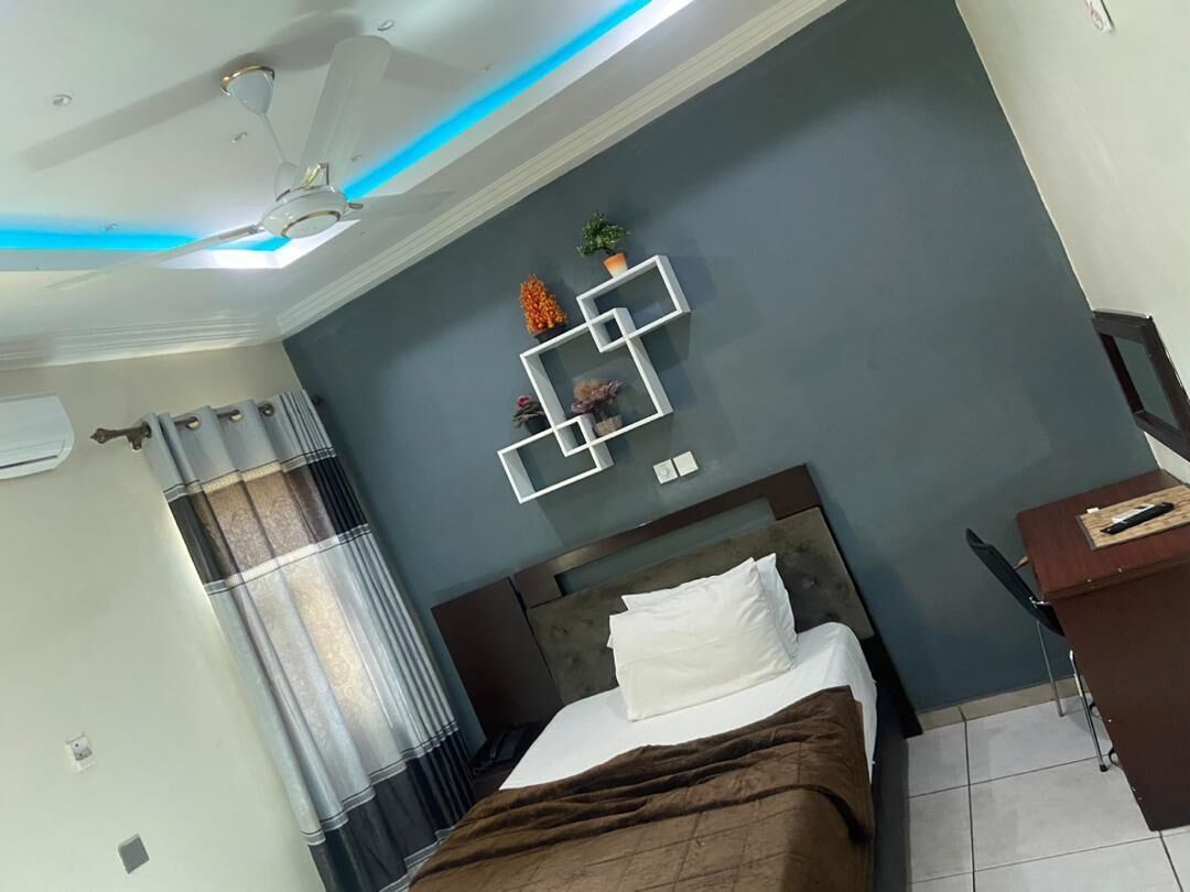 Ein Hotelzimmer mit einem Bett, einem Schreibtisch, einem Deckenventilator und einem an der Wand befestigten Regal mit Dekorationen.