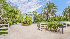 A gated entrance with a mailbox, a pathway leading to a building, and lush tropical vegetation.