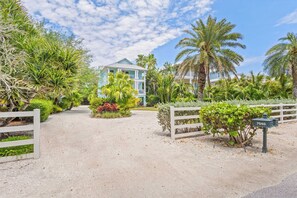 A gated entrance with a mailbox, a pathway leading to a building, and lush tropical vegetation.
