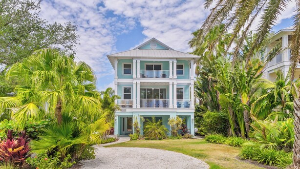 A two-story house with a balcony, surrounded by lush tropical vegetation.
