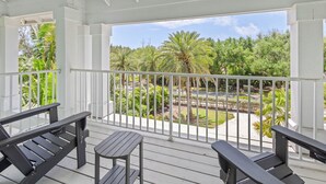 A covered outdoor area with a white railing, wooden benches, and a view of a landscaped garden with palm trees.