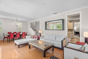 A modern living room with a sofa, coffee table, dining table, and chairs. A staircase is visible in the background. - Aqua Bay 3BR by RVA-Poolside Luxury, Pets Too (Longboat Key)