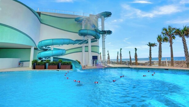A swimming pool with a water slide structure, palm trees, and a clear sky. - Turquoise Place 1807C by Liquid Life (Orange Beach)