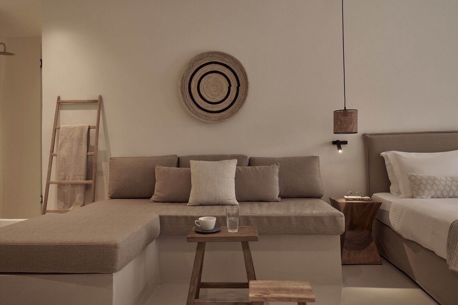 A modern bedroom with a sofa, a bed, a small table with a cup and glasses, a ladder, and a wall-mounted light fixture.