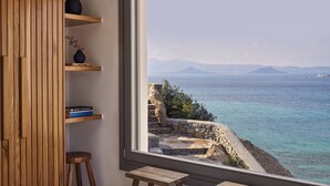 A room with a large window overlooking a coastal view, featuring a stone staircase leading to a cliff.