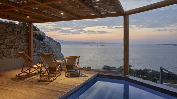 A wooden deck with a pool and two wooden chairs overlooking a body of water.