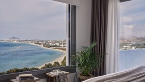 A bedroom with a large window overlooking a beach and town.