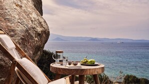 A wooden lounge chair and a small round table with a view of the sea and distant mountains.