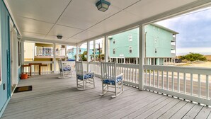 A covered porch with white railings and rocking chairs, overlooking a street with buildings. - ⛱️The Beach House-Cozy Cottage w/ Ocean views!⛱️ (Carolina Beach)