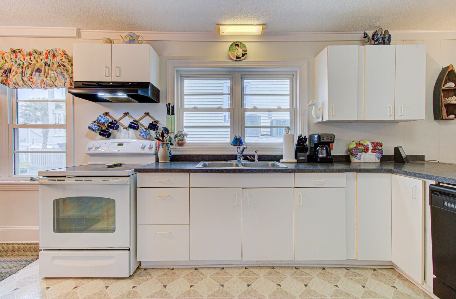 Una cocina con armarios blancos, una estufa, un lavaplatos y una ventana con persianas.