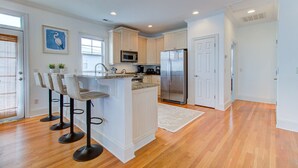 Una cocina moderna con armarios blancos, un refrigerador de acero inoxidable, un microondas y una zona de bar con taburetes.