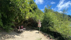 A sandy beach with a row of beach chairs and a striped umbrella, surrounded by dense greenery and a clear blue sky. - River Time ~ Come Stay on the River! Access to Park, Riverfront, In Town (Monte Rio)