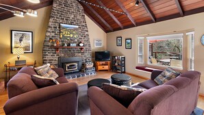 A cozy living room with a stone fireplace, comfortable seating, and a TV. - River Time ~ Come Stay on the River! Access to Park, Riverfront, In Town (Monte Rio)