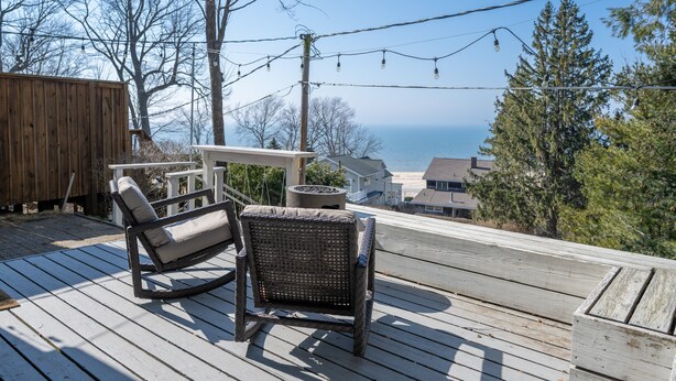 A wooden deck with wicker chairs and a table, overlooking a body of water and houses. - Cozy Cottage across from Grand Haven Beach (Grand Haven)