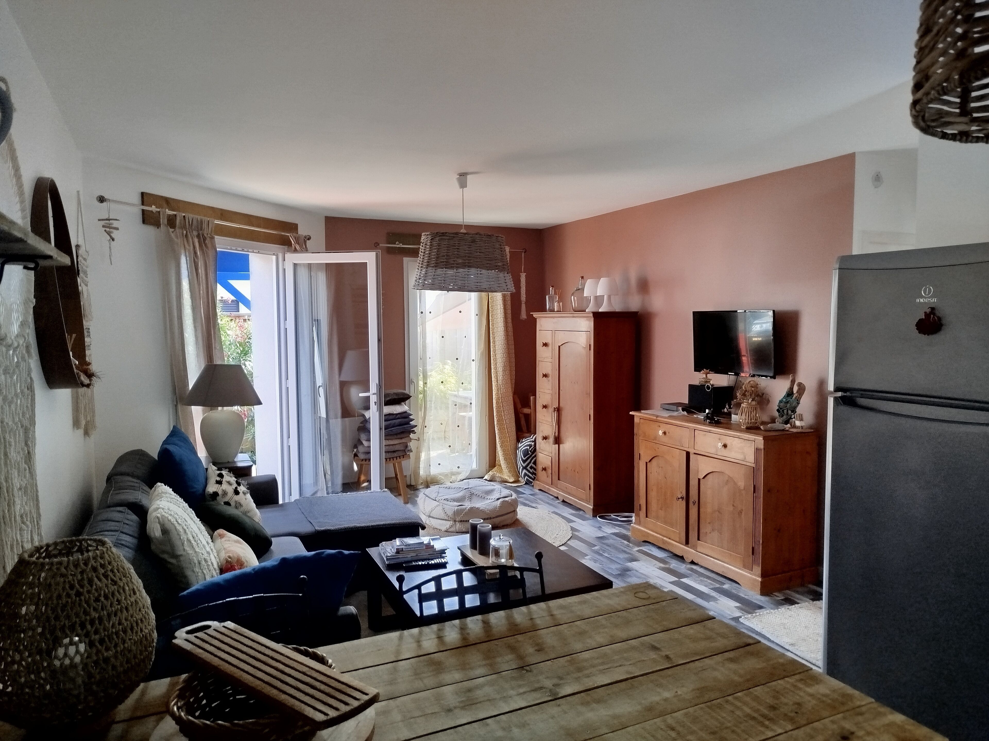 Ein gemütliches Wohnzimmer mit Sofa, Couchtisch und Fernseher. Es gibt eine Küchenzeile mit Kühlschrank, Schränken und einem Esstisch.