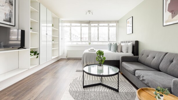 A modern living room with a grey sofa, a glass coffee table, and a TV on a white cabinet.