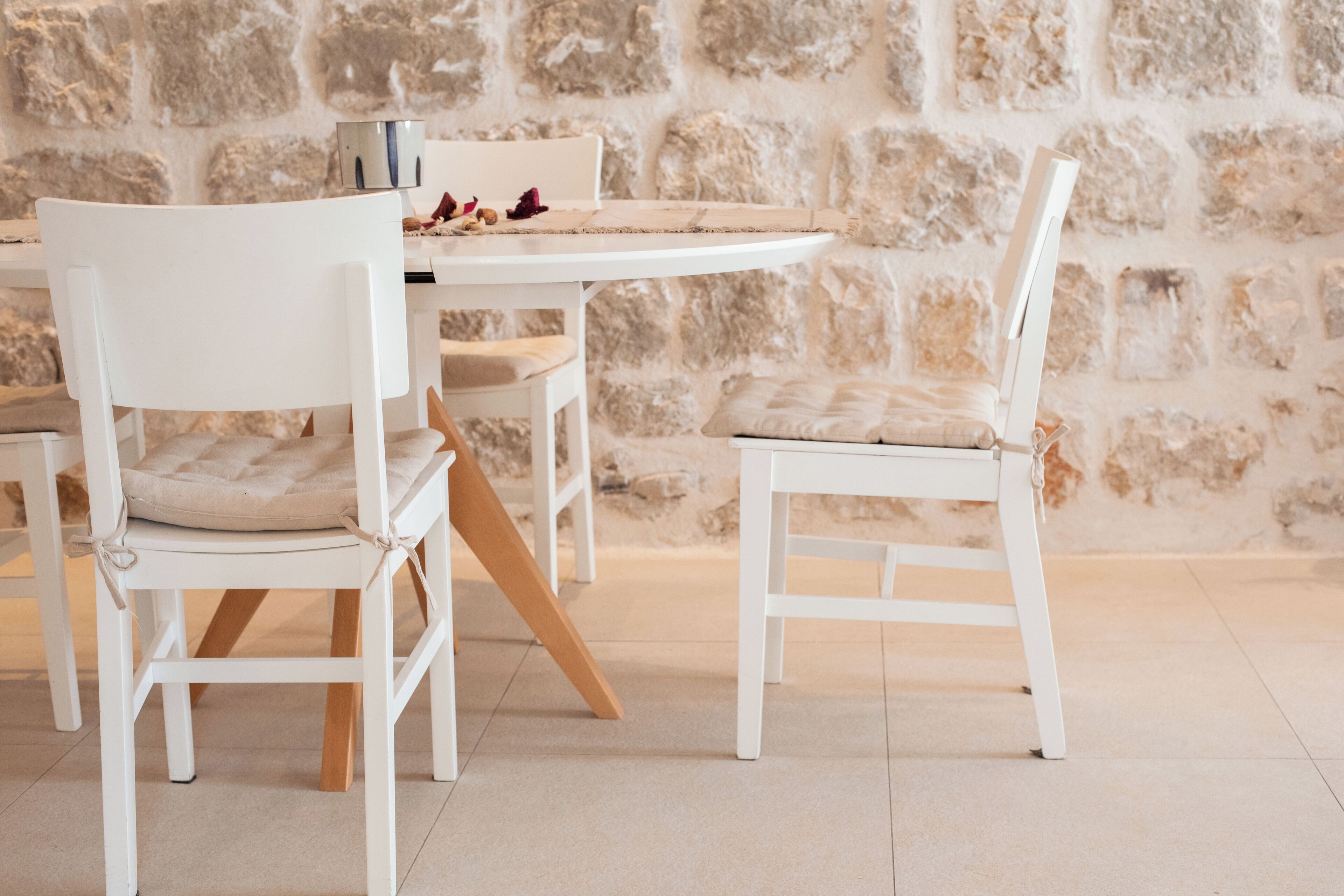 Un área de comedor con sillas blancas y una mesa, frente a una pared de piedra.