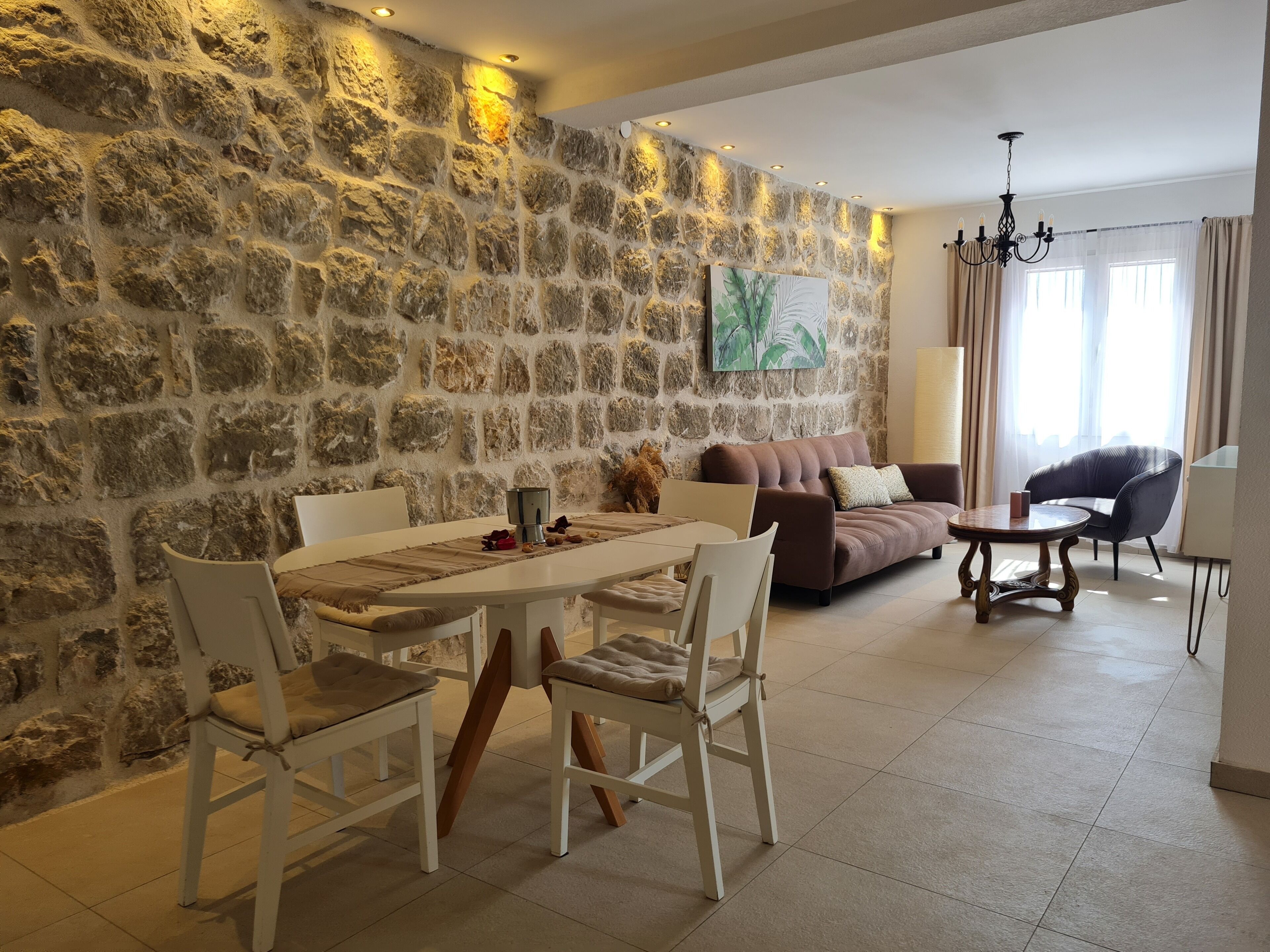 Un soggiorno con parete in pietra, un tavolo da pranzo con sedie, un divano, un tavolino e un lampadario.