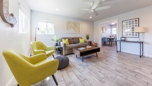 A living room with a sofa, two yellow armchairs, a coffee table, and a ceiling fan. - Carlsbad Beach Bungalows - 4BRs, Outdoor Living, Walk to Beach, Pet-Friendly (Carlsbad)