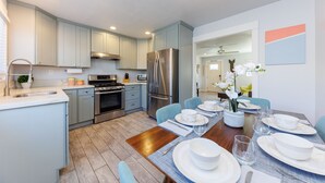 A modern kitchen with light blue cabinets, stainless steel appliances, and a dining area set for four. - Carlsbad Beach Bungalows - 4BRs, Outdoor Living, Walk to Beach, Pet-Friendly (Carlsbad)
