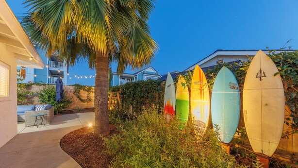 A house with a patio, a palm tree, and surfboards leaning against a wall. - Carlsbad Beach Bungalows - 4BRs, Outdoor Living, Walk to Beach, Pet-Friendly (Carlsbad)