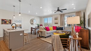 Ein modernes Apartment mit Küche, Essbereich und Wohnzimmer. Es verfügt über einen Deckenventilator, Pendelleuchten und ein großes Fenster mit Blick.