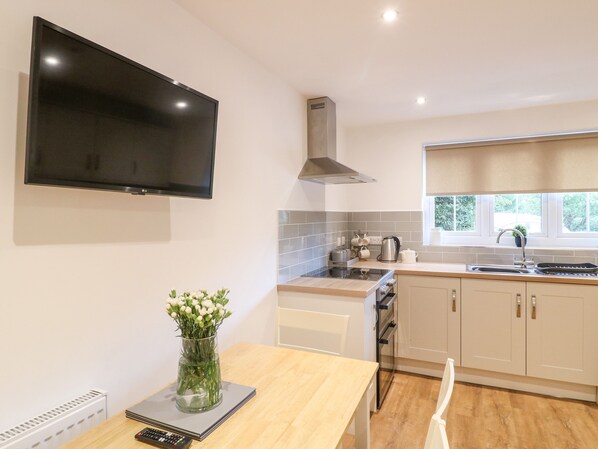 A modern kitchen with a flat-screen TV, a stainless steel range hood, a window with a view, and a vase with flowers on the counter.