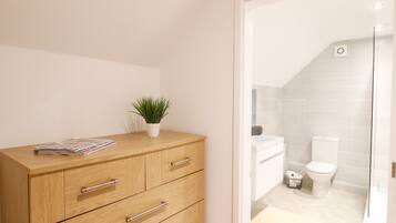 Un baño moderno con un mueble de madera, una pequeña planta en maceta y un inodoro blanco.