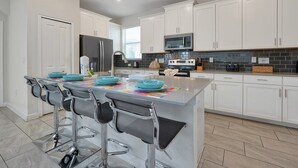 A modern kitchen with white cabinets, stainless steel appliances, and a central island with bar stools. - 5 Bed In Champions Gate, Modern Decor, Kid Themed Rooms, Game Room, Gated Resort! 5 Bedroom Home by RedAwning (Davenport)
