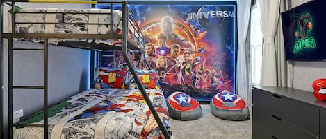 A room with bunk beds, a large superhero-themed poster, bean bags, and a TV on the wall.