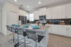 A modern kitchen with white cabinets, stainless steel appliances, and a central island with bar stools. - 5 Bed In Champions Gate, Modern Decor, Kid Themed Rooms, Game Room, Gated Resort! 5 Bedroom Home by RedAwning (Davenport)